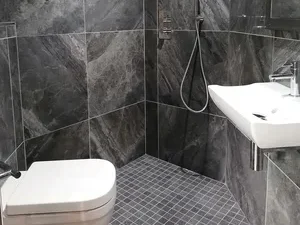 Modern bathroom featuring grey stone tiles, shower, sink, and toilet.