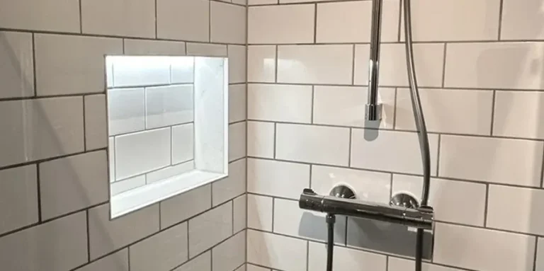 Modern shower with white tiled walls and a recessed shelf.